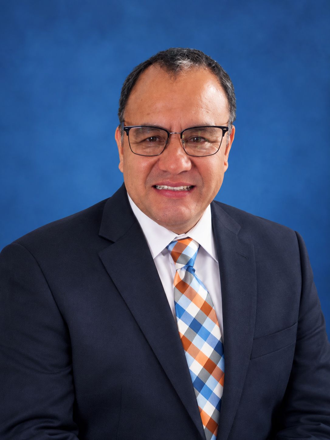 Jorge Carrillo, dueño y conductor de US1 Driver, sonriendo con traje azul marino y corbata a cuadros.